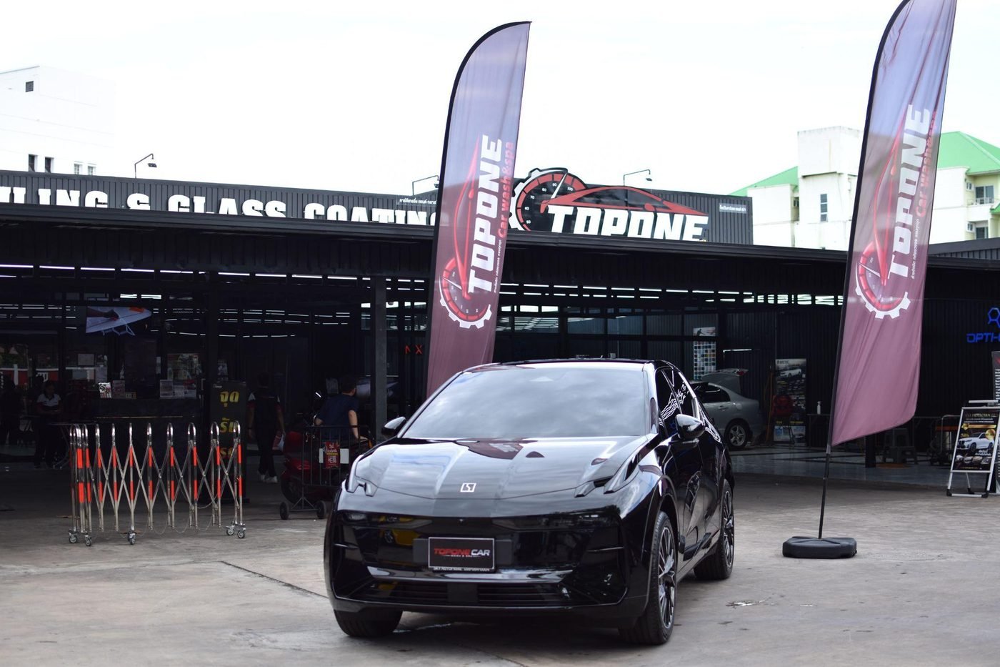 รถยนต์ไฟฟ้าสีดำจอดหน้าร้าน TOPONE Car Wash & Spa พร้อมธงโลโก้ร้านสองข้าง